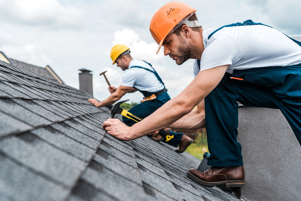 2 roof technicians installing shingles on a sloped roof