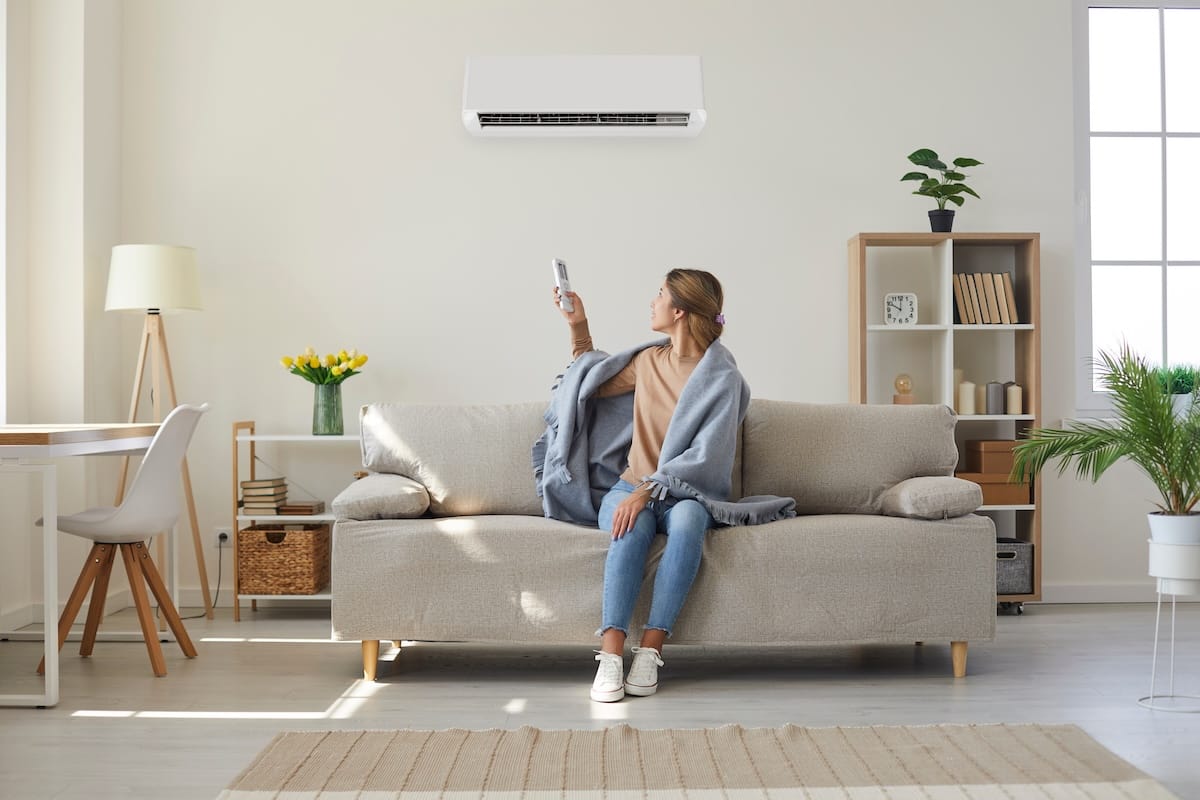 Woman enjoying cool fresh air in her living room with air conditioner on the wall