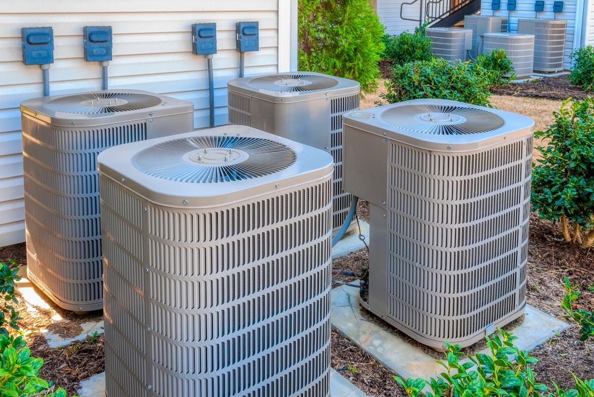 Horizontal shot of four air conditioning units outside of an upscale apartment complex.