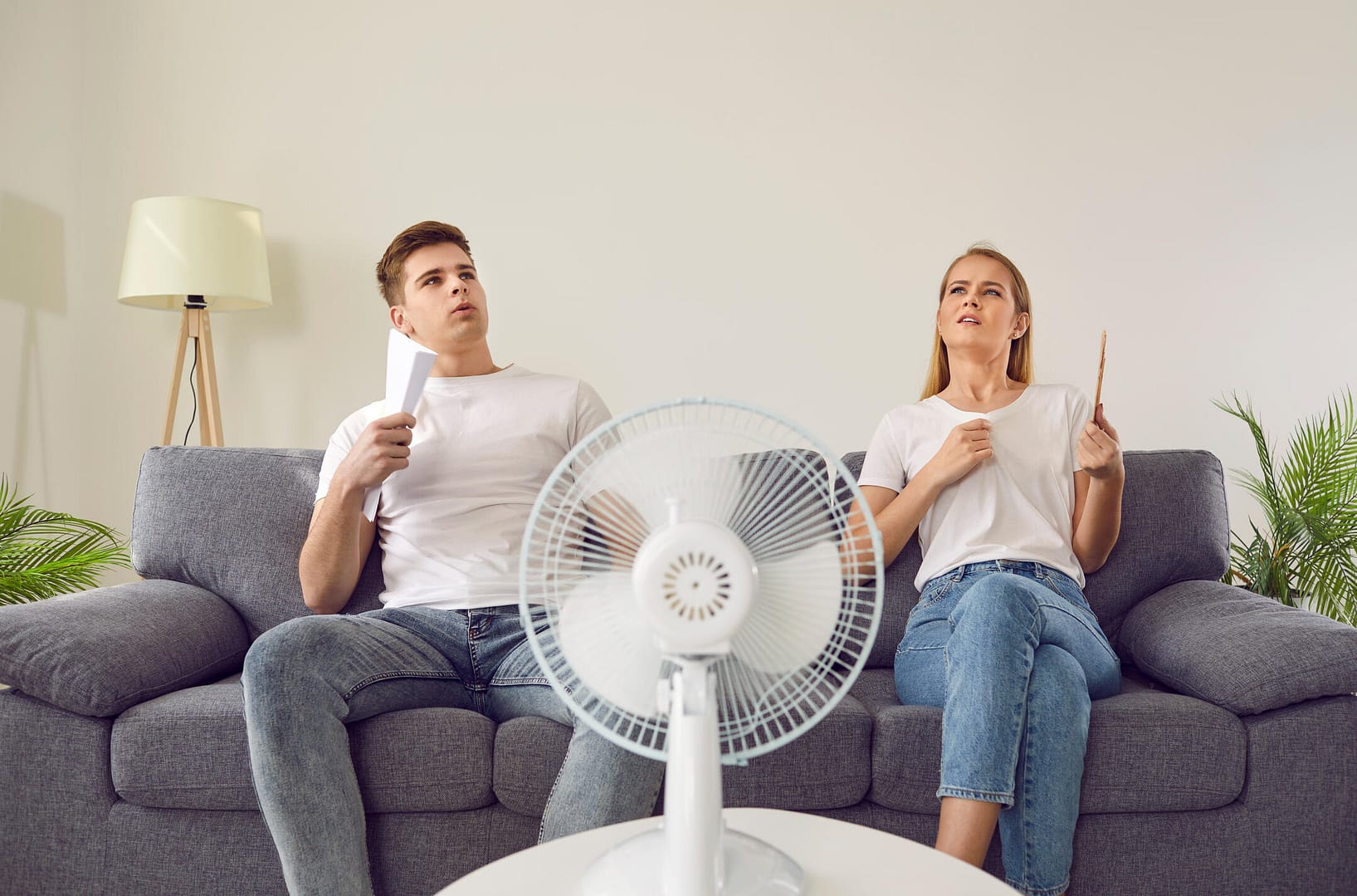 ac not turning on-couple sitting on couch in front of a fan, too hot inside home