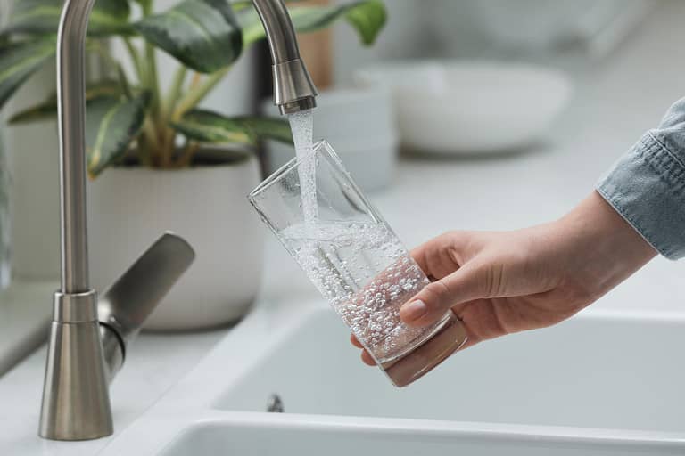 best under sink water filter-woman filling up a drinking glass with water from the kitchen faucet