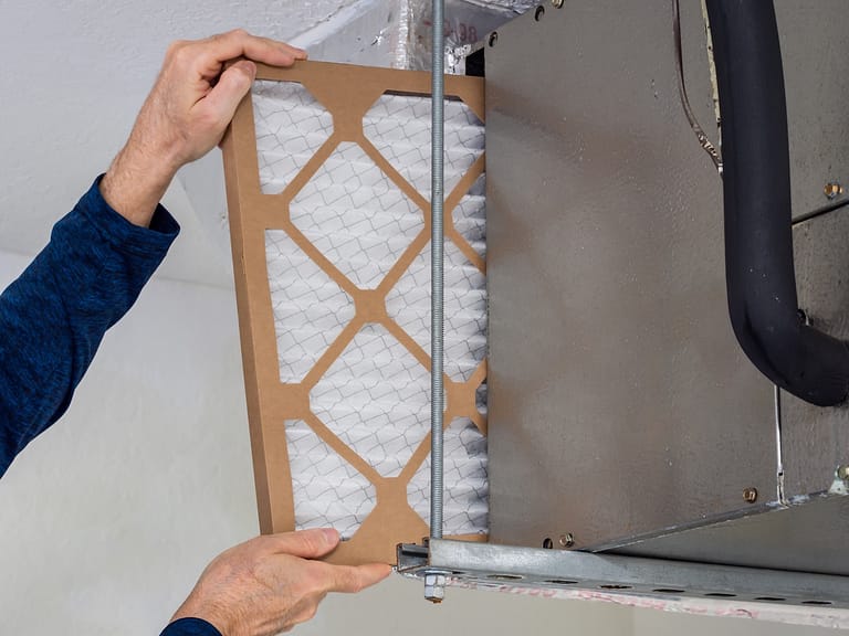 HVAC service technician changing dirty indoor air filter in residential heating and air conditioning system. Home air duct ventilation system maintenance for clean air.