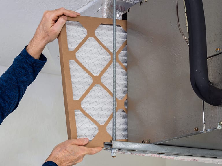 HVAC service technician changing dirty indoor air filter in residential heating and air conditioning system. Home air duct ventilation system maintenance for clean air.