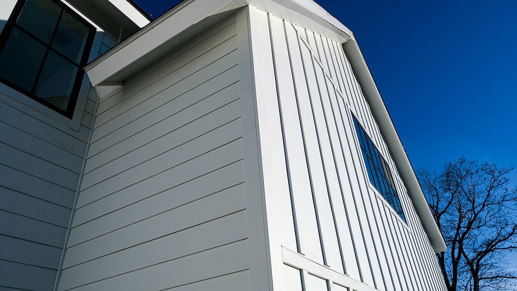 low-angle architectural photograph of a modern farmhouse with Hardie board siding in a crisp white finish, featuring a combination of horizontal lap and vertical board and batten panels.