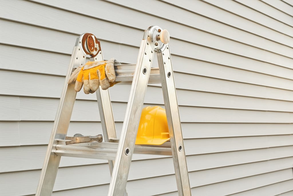 Stepladder, hardhat, gloves and hammer with house siding background
