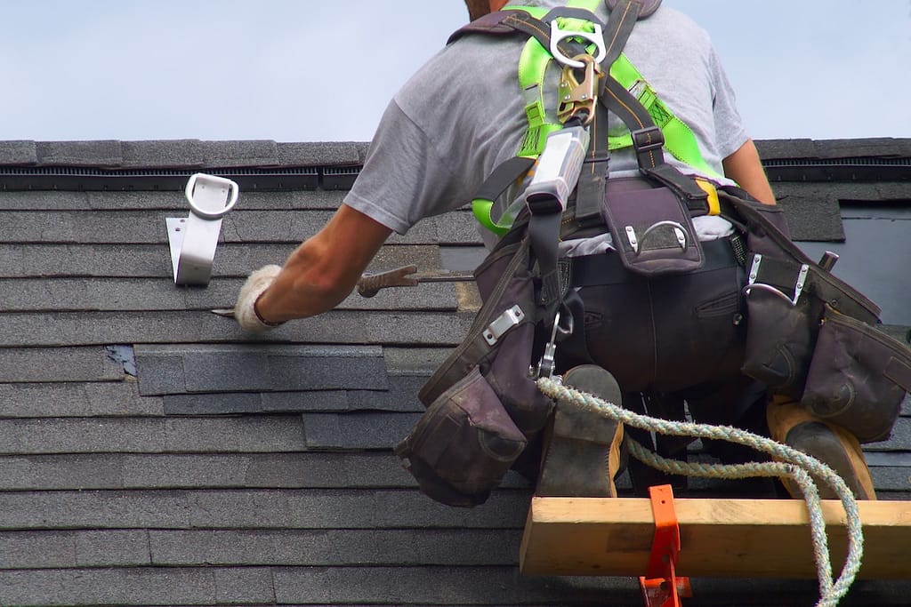 roofer making repairs while strapped in to a safety harness