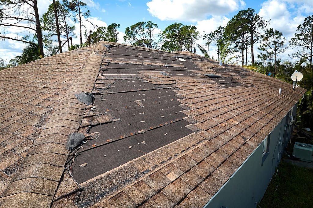 Damaged house roof with missing shingles after storm