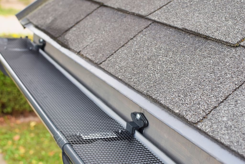 Plastic guard over new dark grey plastic rain gutter on asphalt shingles roof.