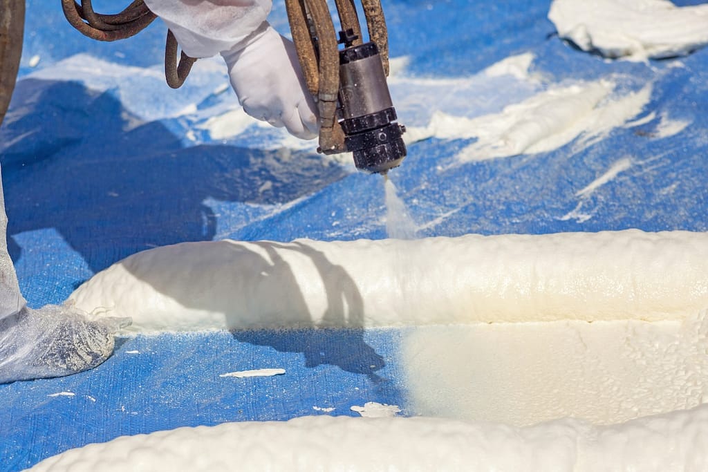 Technician dressed in a protective white uniform spraying foam insulation