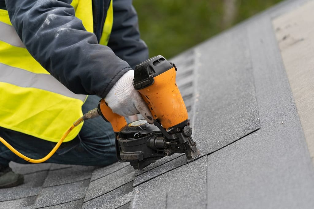 roofer using nail gun to install shingle