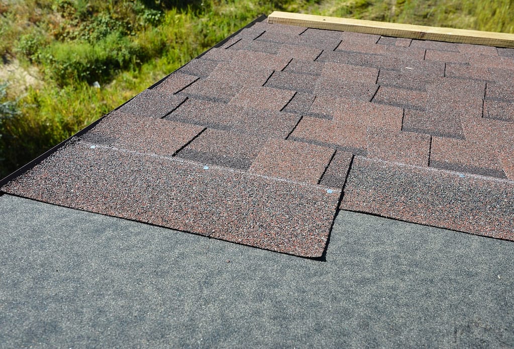 Installing brown dimensional asphalt roof shingles on the underlayment, water-resistant, waterproof protection barrier material on the rooftop of the house construction during house repairing.