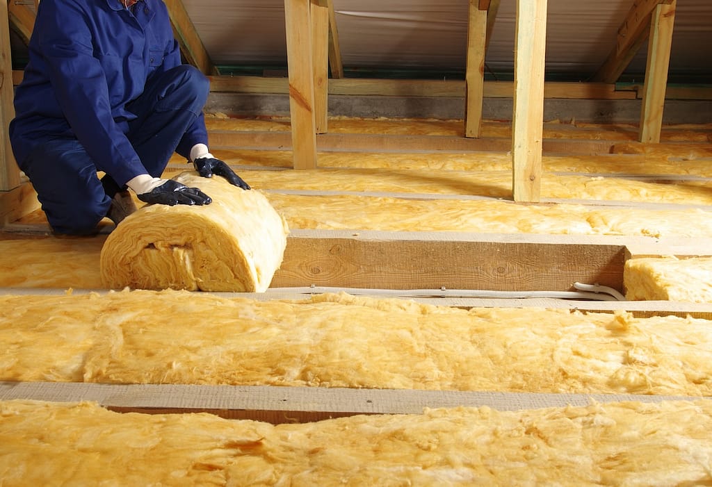 Construction worker thermally insulating house attic with glass wool