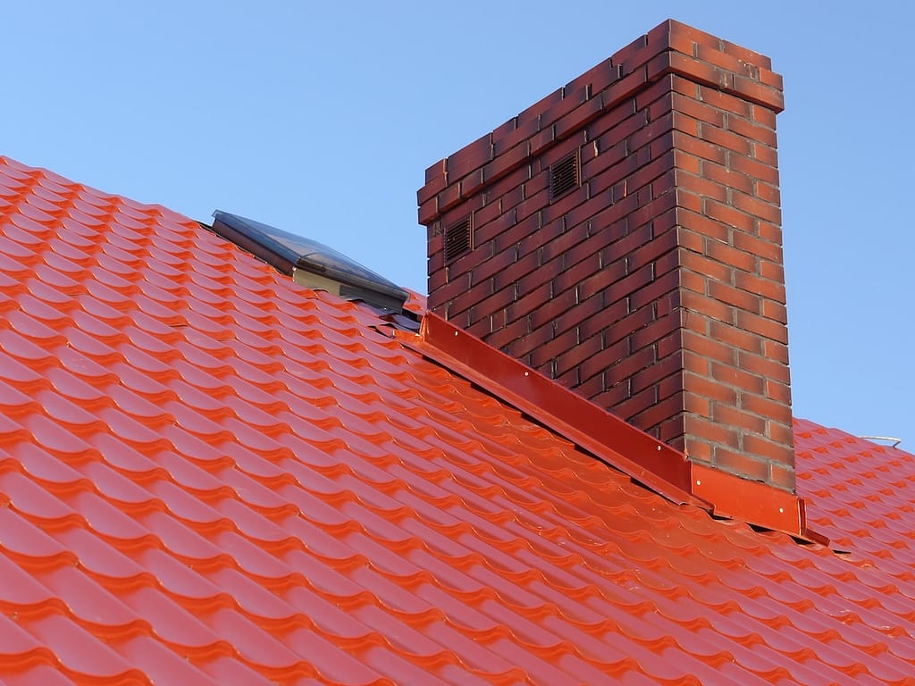 Closeup of red roof metal flashing with brick-made chimney