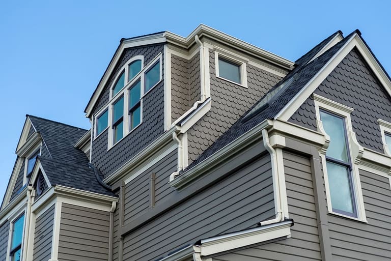 Large historic home with grey siding under blue sky