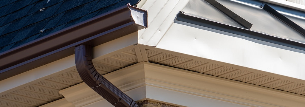 Perforated soffit vents along a beige roof eave with brown gutter and downspout