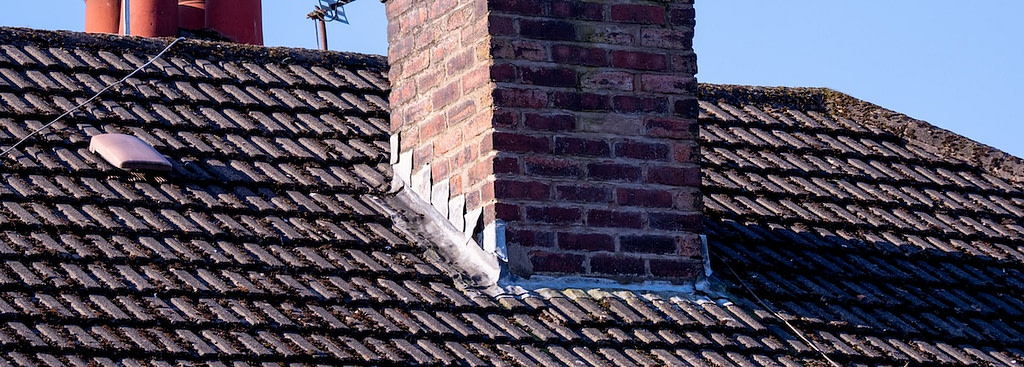 Brick chimney with metal flashing repair on a tiled roof, showing weathered joint sealing