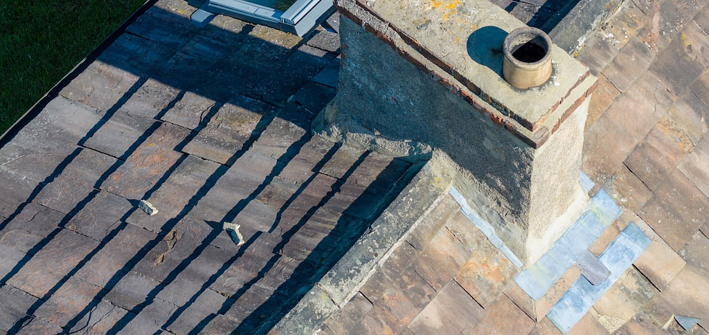 Concrete chimney with metal flashing on a slate roof, showing weathered stone tiles