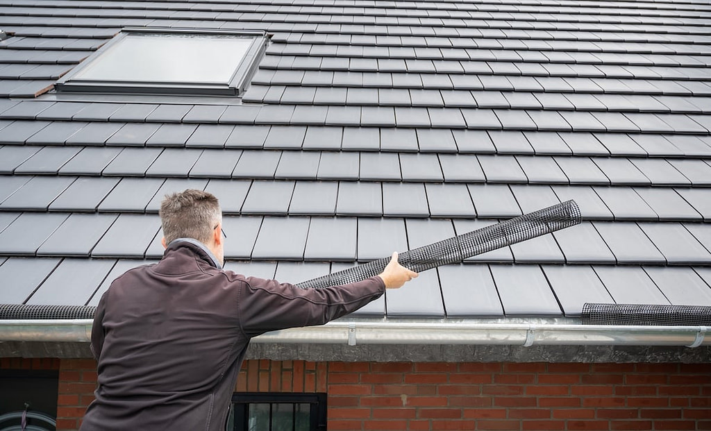 Man puts a gutter mesh to the rain gutter to protect the gutter from leaves.