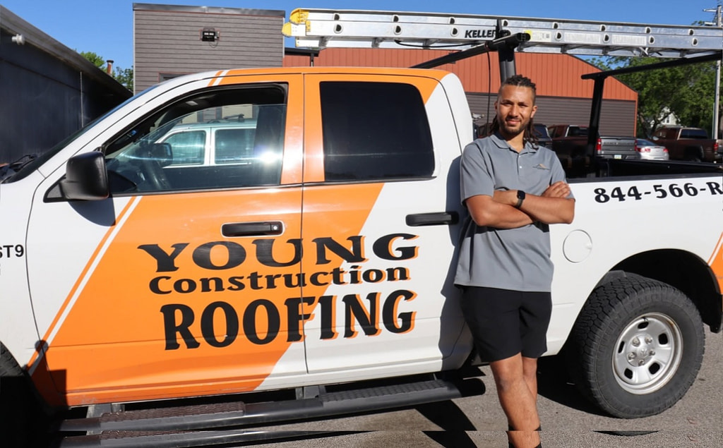 Roofing contractor standing beside a branded Young Construction Roofing service truck