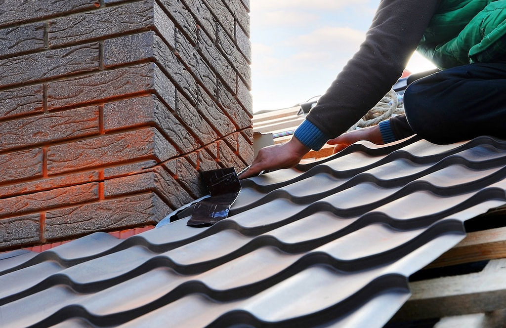 Roofer repairing metal roofing next to chimney on roof