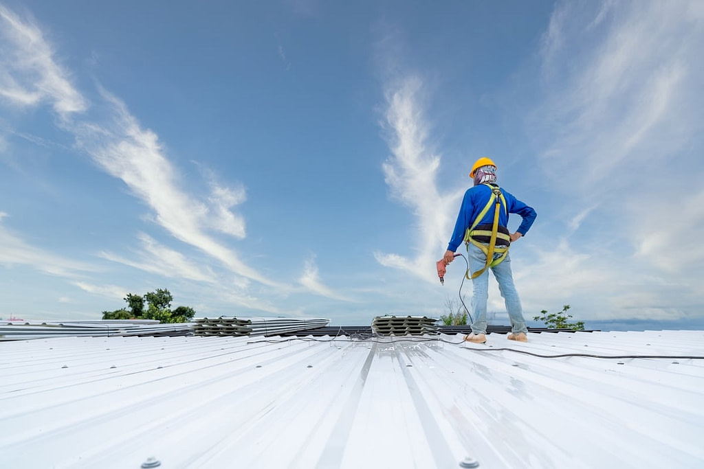 A Roofer using electric drill nail gun installing commercial roofing materials