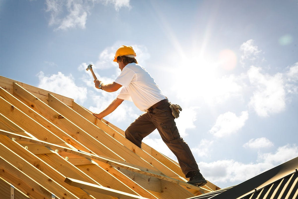 roofer or Carpenter working on Roof on roofing project backlit by sun