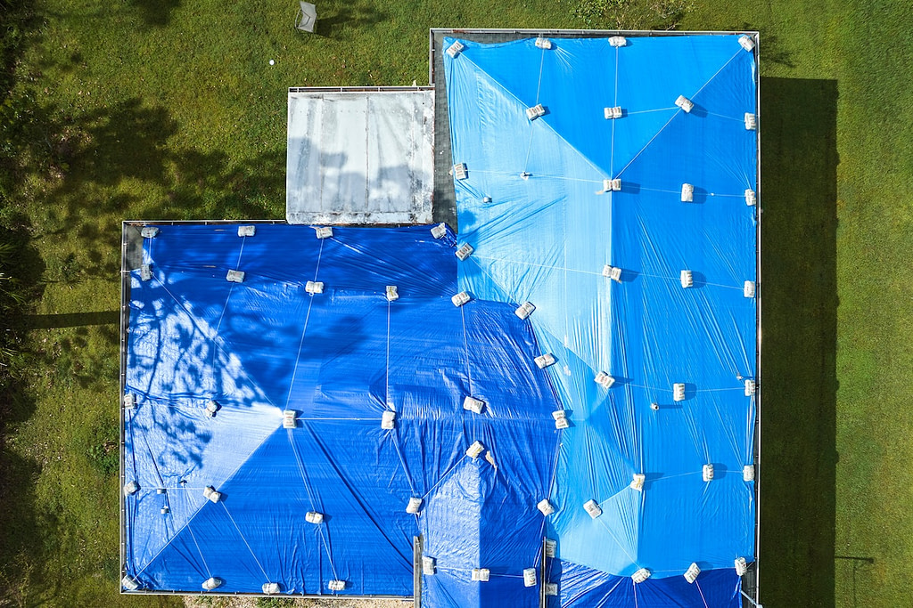 Top view of leaking house roof covered with protective tarp sheets against rain water leaks until replacement of asphalt shingles