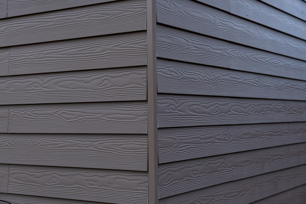 The corner of a house features gray horizontal siding with a wood grain texture