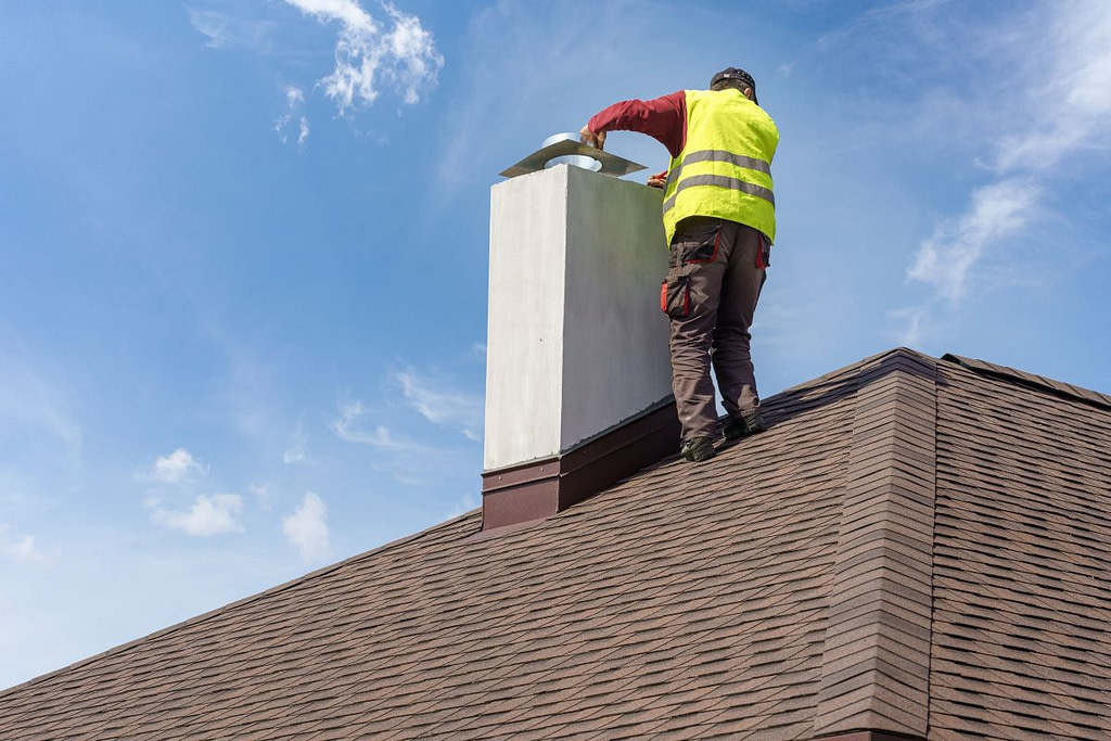 Man installing chimney cap on roof top of new house under construction