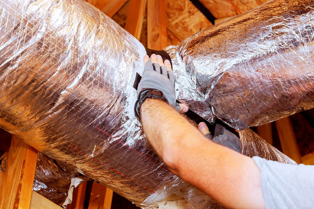 Contractor worker adjusts insulation around ductwork in residential attic, ensuring proper sealing efficiency