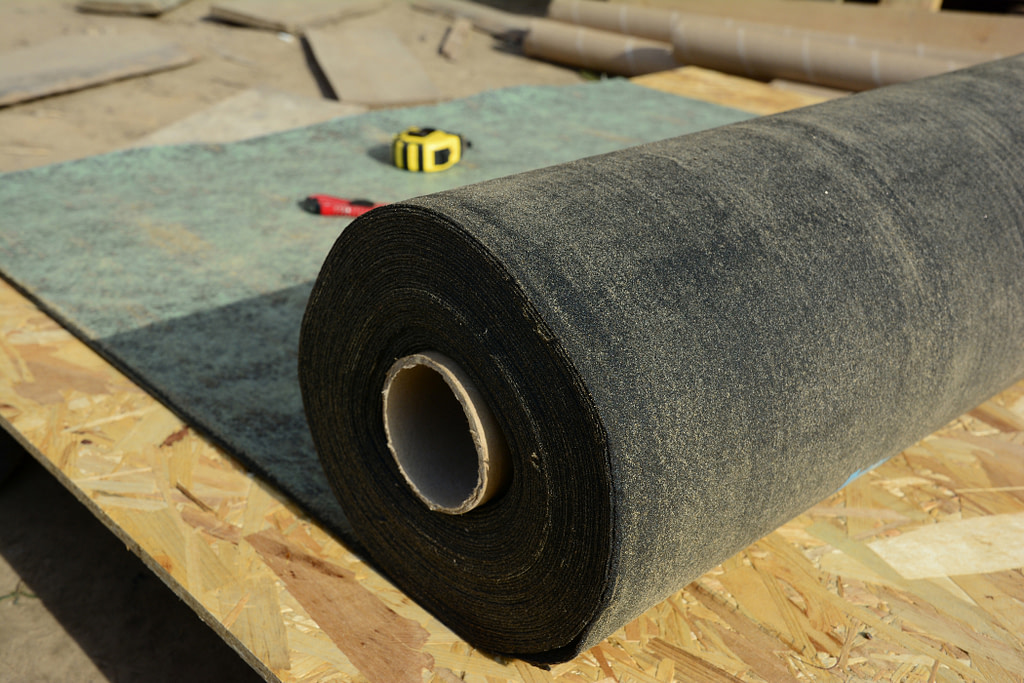 roof underlayment types Unrolling waterproofing, water-resistant felt, bituminous roofing underlayment on the roof sheathing, roof deck before asphalt shingles installation while roofing construction.