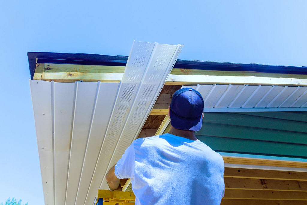 vinyl soffit installation worker cutting fascia Mounting vinyl soffit plastic boards to roof rafters on ceiling house