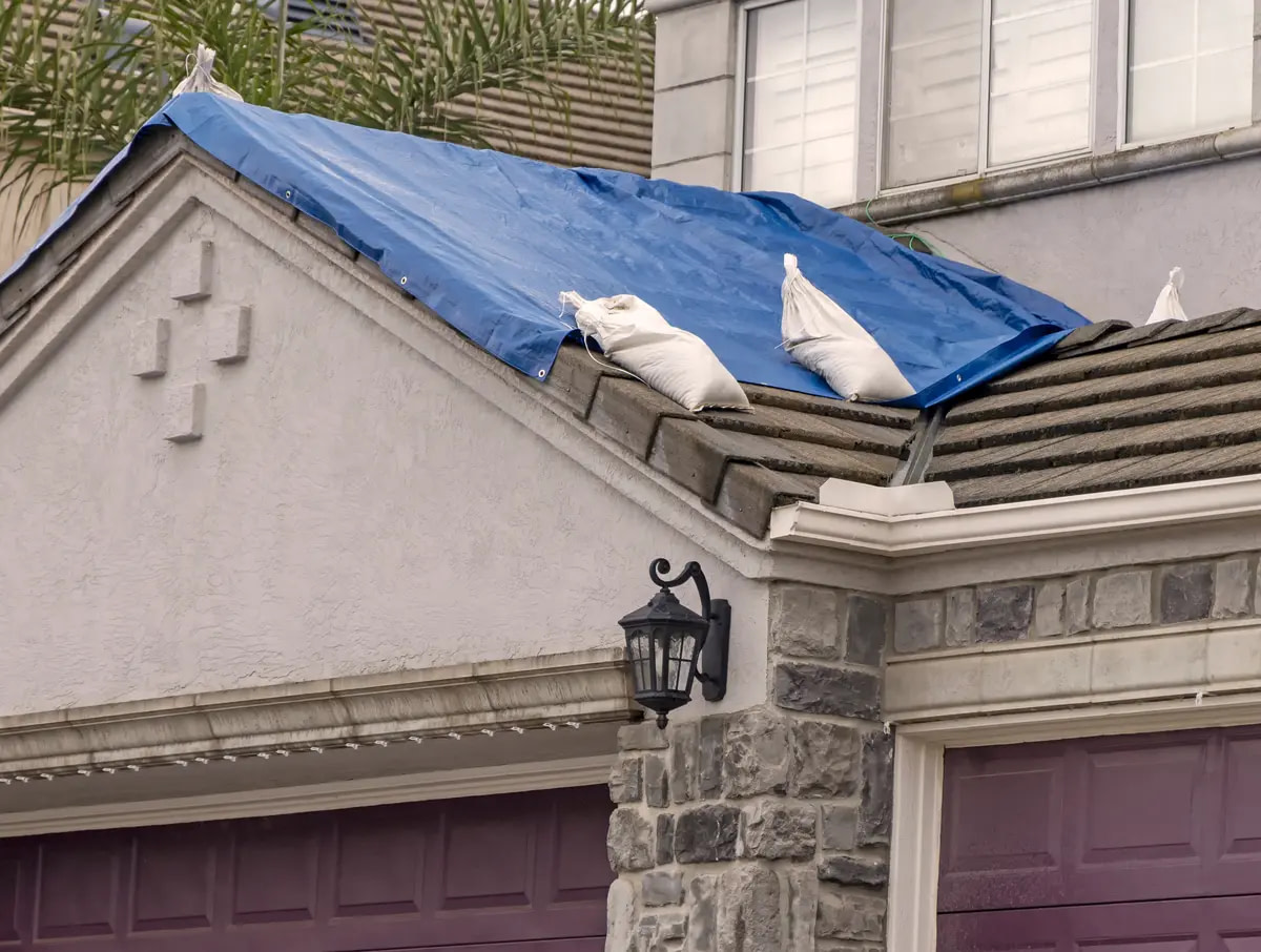 Tarp covering a home’s roof with sandbags after roof storm damage