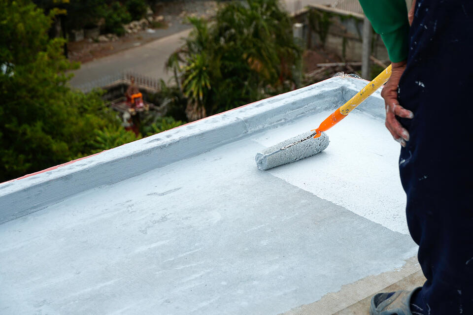 roof coating-man painting white coating on flat residential roof with paint roller