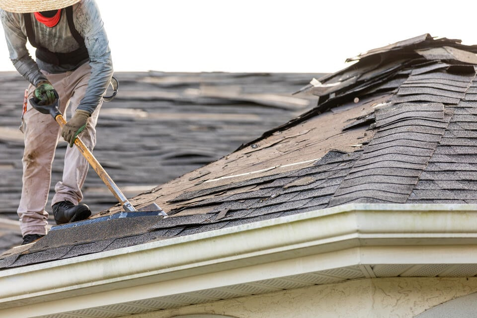 roof tear off-person wearing protective gear shoveling off old shingle roof