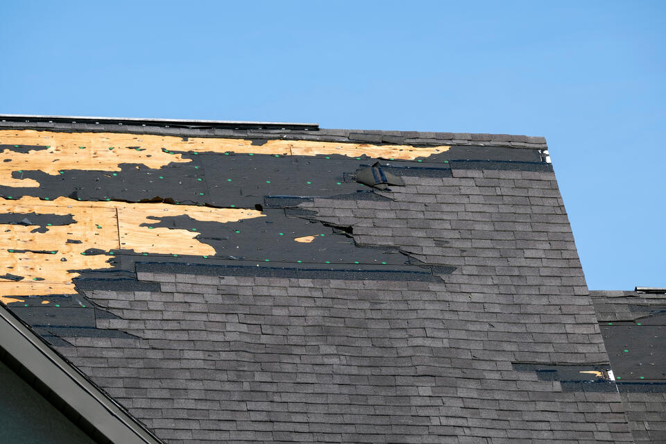 missing shingles-shingle roof house with large patch of missing shingles and underlayment with exposed sheathing