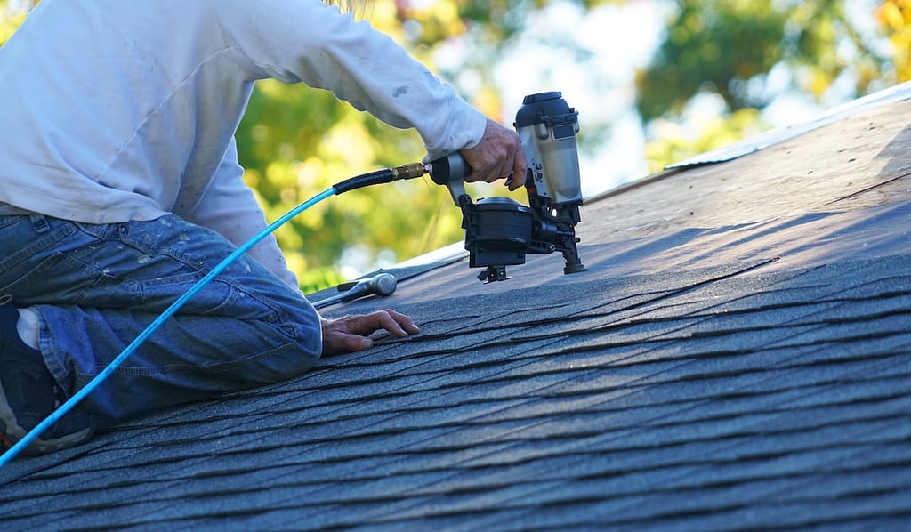 Handyman using a nail gun to secure asphalt shingles to roof
