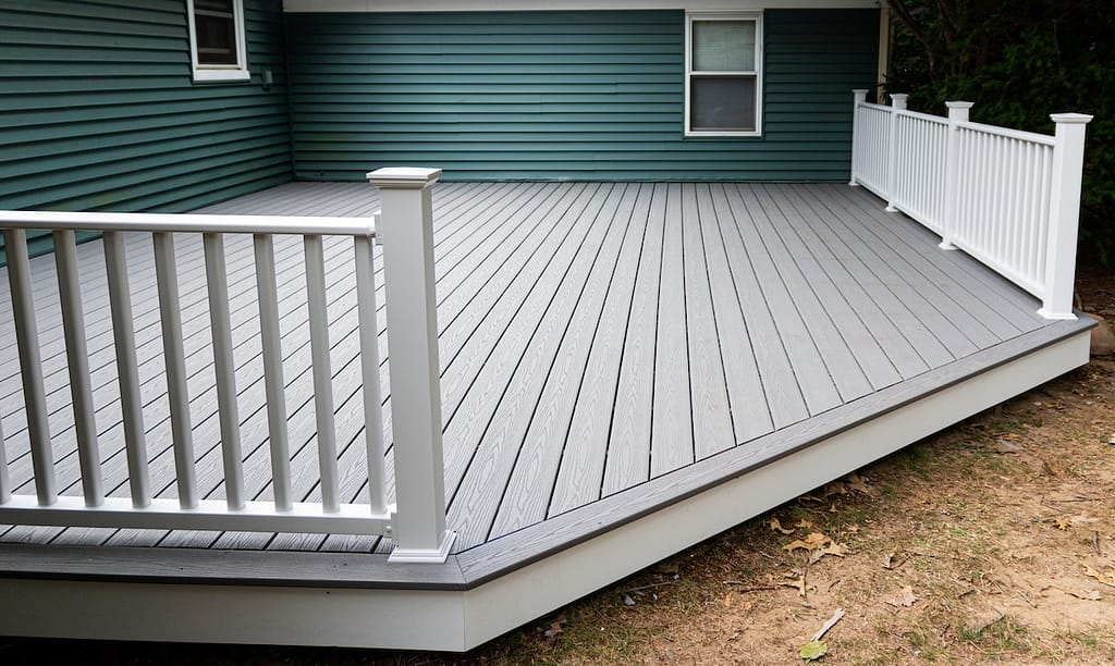 New composite deck on the back of a house with green vinyl siding.with whie railings.