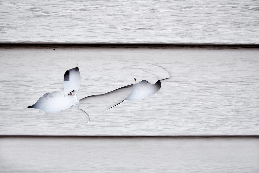 Close up of a cracked and broken beige vinyl siding of a house