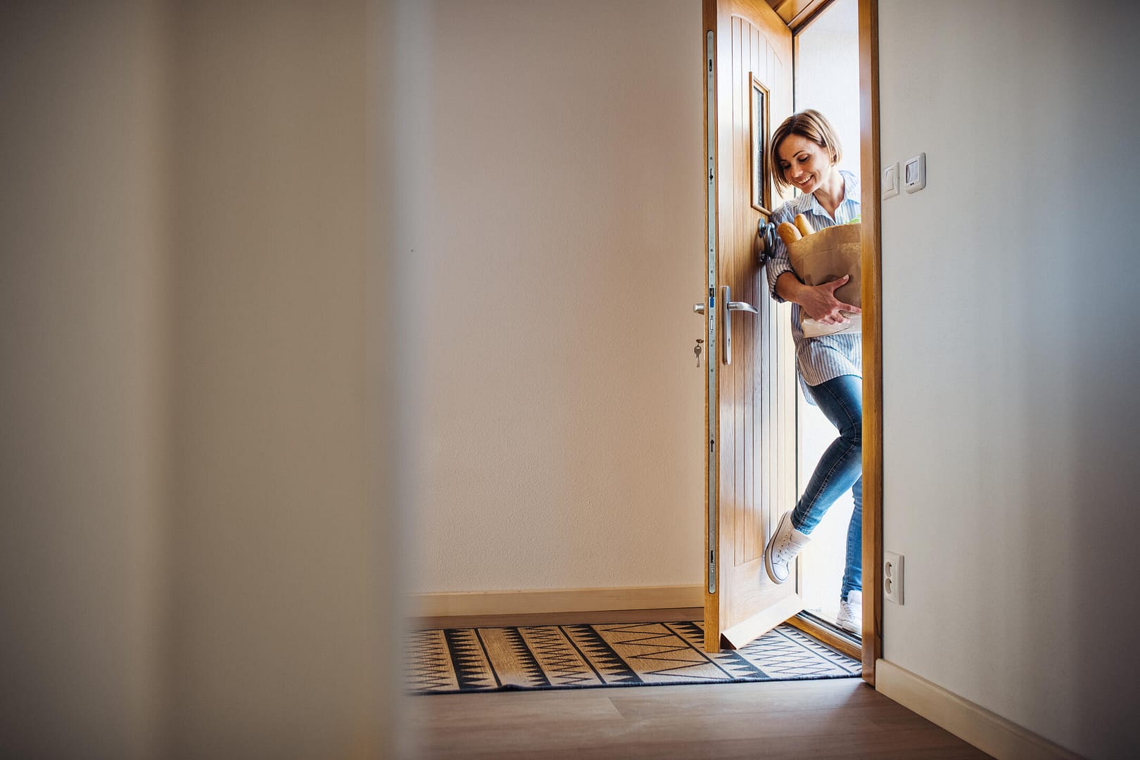 front door styles-woman entering her home through the front door with groceries