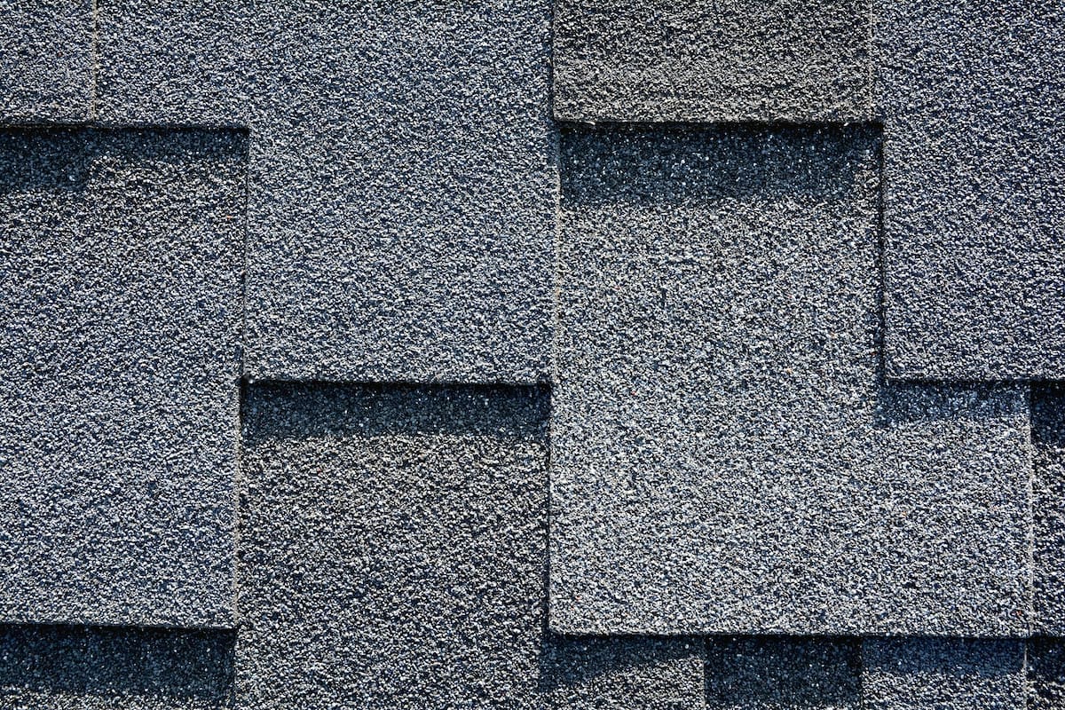 Close-up of a textured, gray asphalt shingle roof installed by Houston roof experts. The shingles are overlapping in a uniform pattern, creating a mosaic-like appearance with varying shades of gray. The surface has a grainy texture typical of asphalt roofing materials.