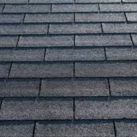 A close-up view of a roof covered with evenly laid, gray asphalt shingles. This illustrates the difference between Architectural Shingles vs 3 Tab, showing the uniformly arranged, textured surface with varying shades of gray.