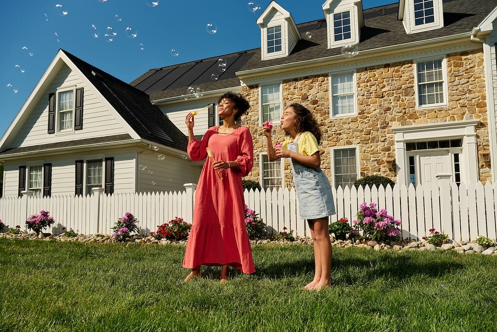 Family blowing bubbles in front of their house. House has GAF Solar Shingles installed on the roof