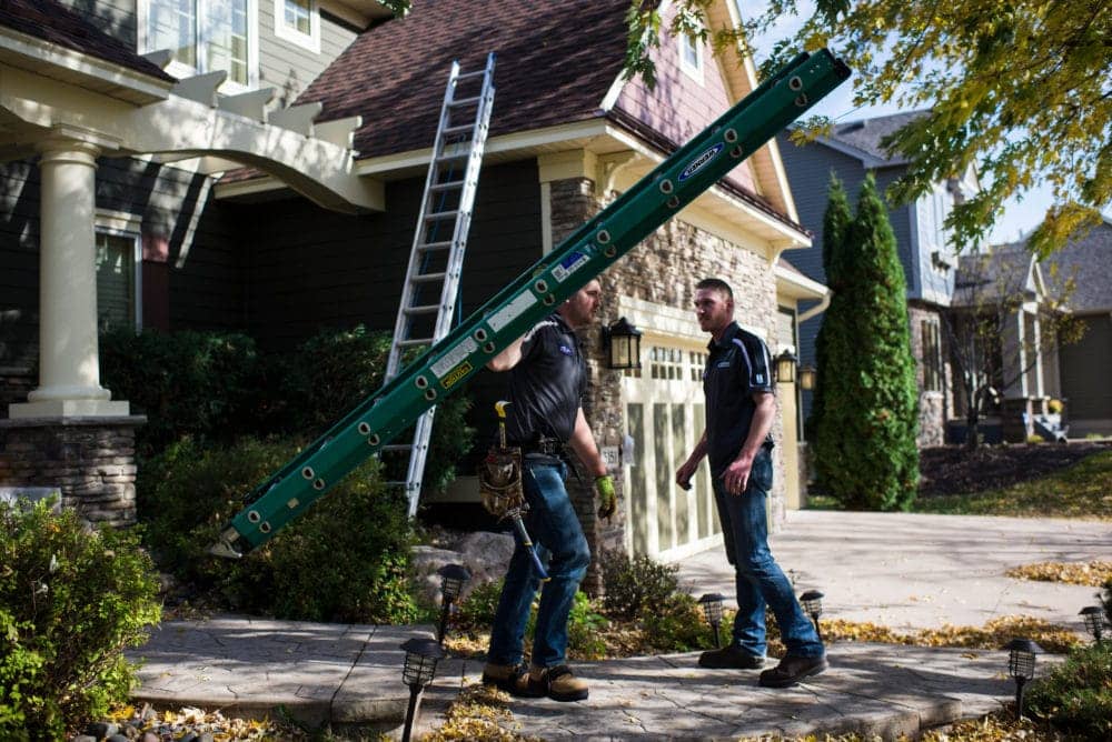 Roofers on site installing roof one holding ladder