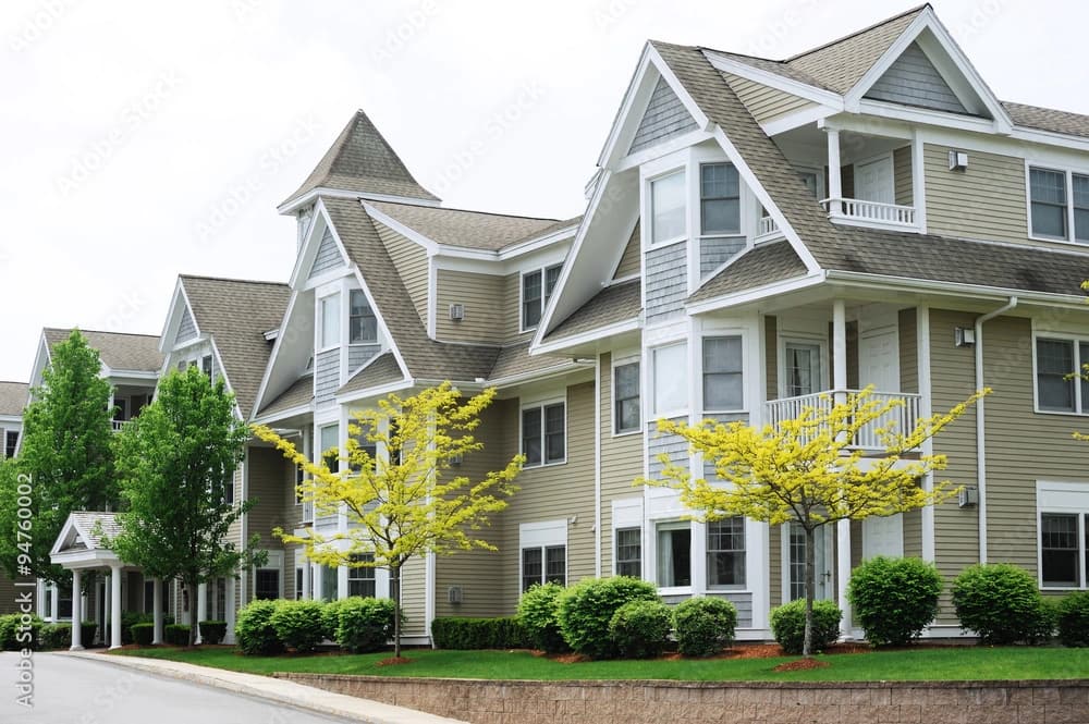 White and tan condos with tall peaked roofs with yellow trees below them