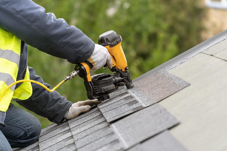 affordable roofing-close up of a roof tech installing roof shingles with a powertool