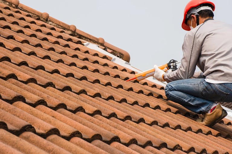 roofer sealing the roof leak using a glue gun with silicone