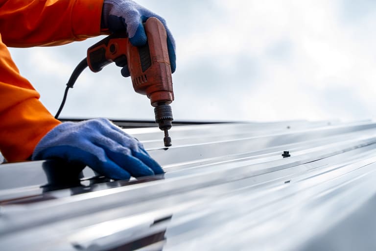 A man drilling into a metal roof on a house, likely for installation or repair purposes.