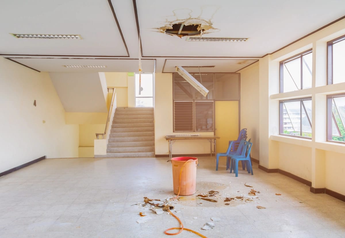 water leaking from ceiling-hole in ceiling from a leak with a bucket on the floor catching drips