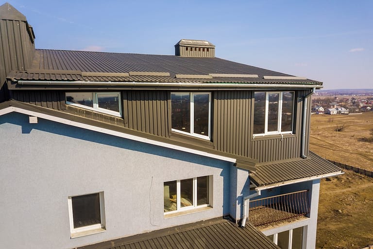 Aerial view of attic annex room exterior with plastic windows, roof and walls covered with brown metal decorative siding planks, new gutter system on top of apartment building.